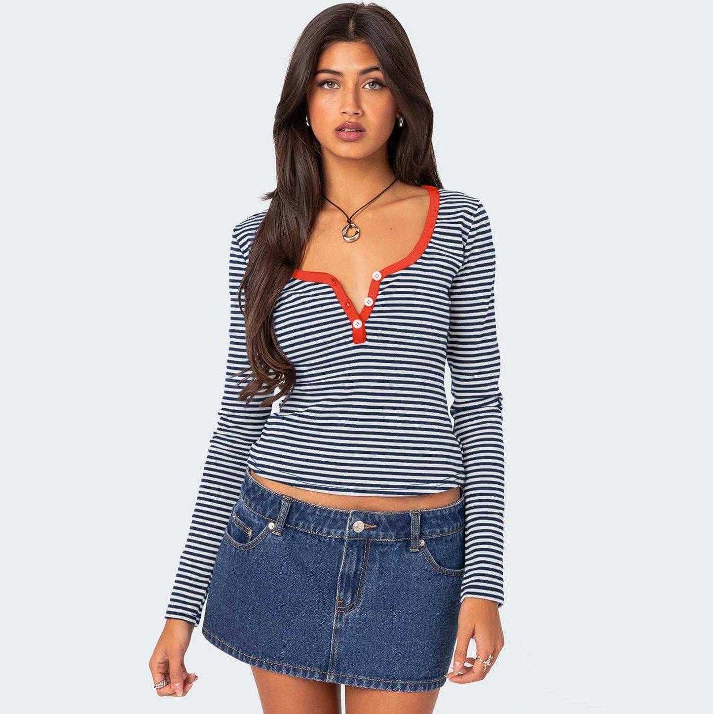 Contrast color striped sweater on woman with red accents and buttoned neckline, paired with denim skirt.